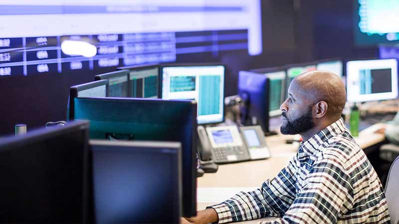 A man monitors data happening on multiple screens on his desk.