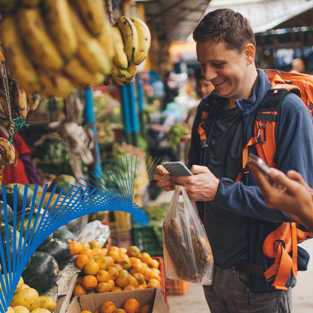 Man buying fruit using his mobile phone at an outdoor market.