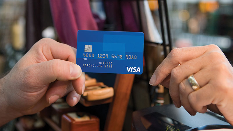 Gambar dua orang yang satu orang menyerahkan kartu kredit Visa kepada orang lain.